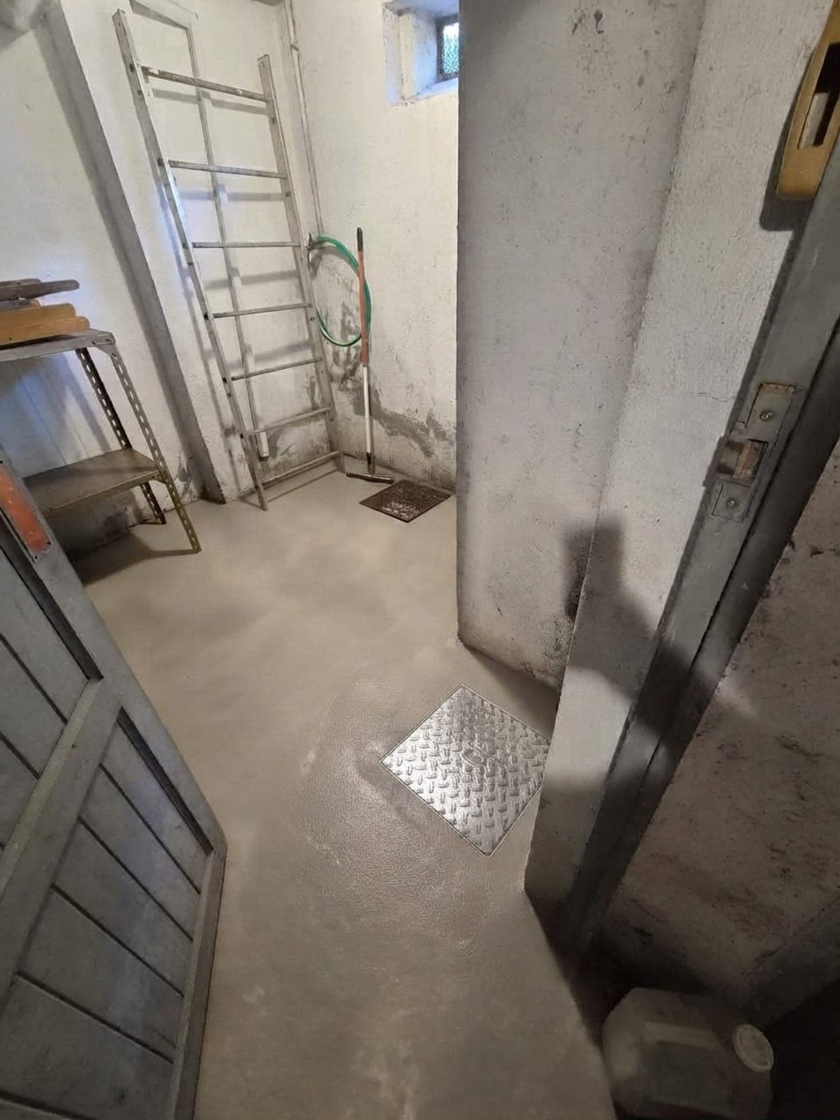 Couloir de sous-sol au sol propre devant une porte bleue, échelle contre le mur et avaloir net