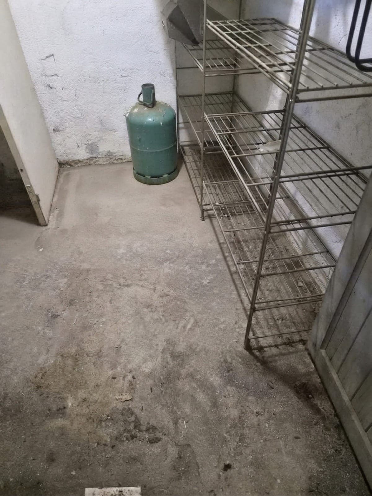 Sous-sol au sol lavé, bonbonne de gaz et étagère métallique dégagées contre le mur blanc