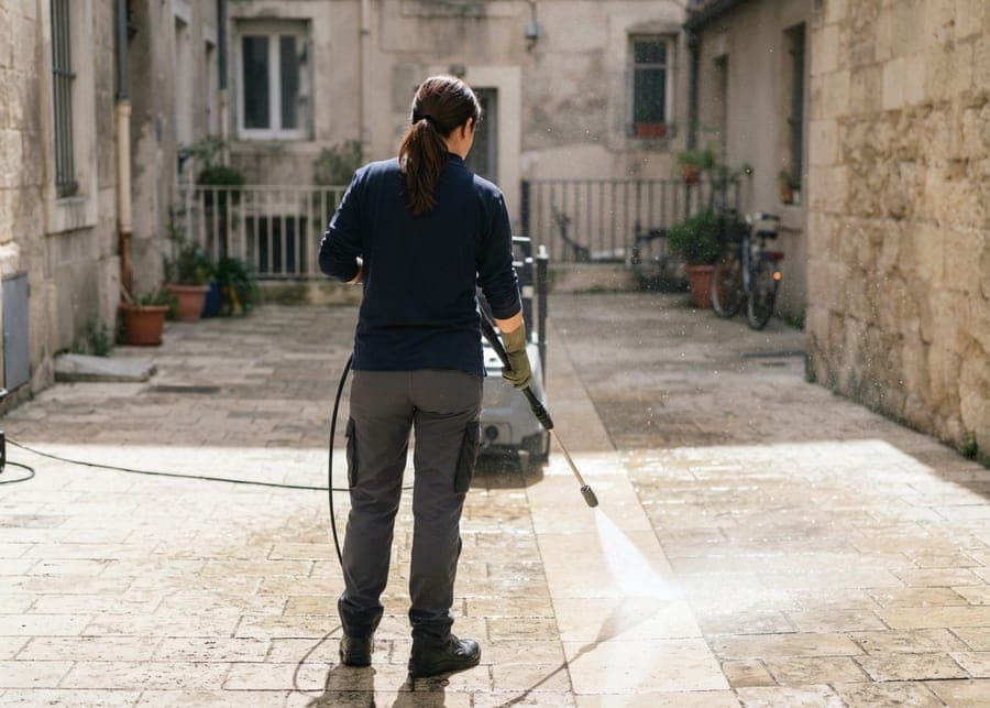 Femme lavant au nettoyeur haute pression les pavés de pierre d'une cour intérieure