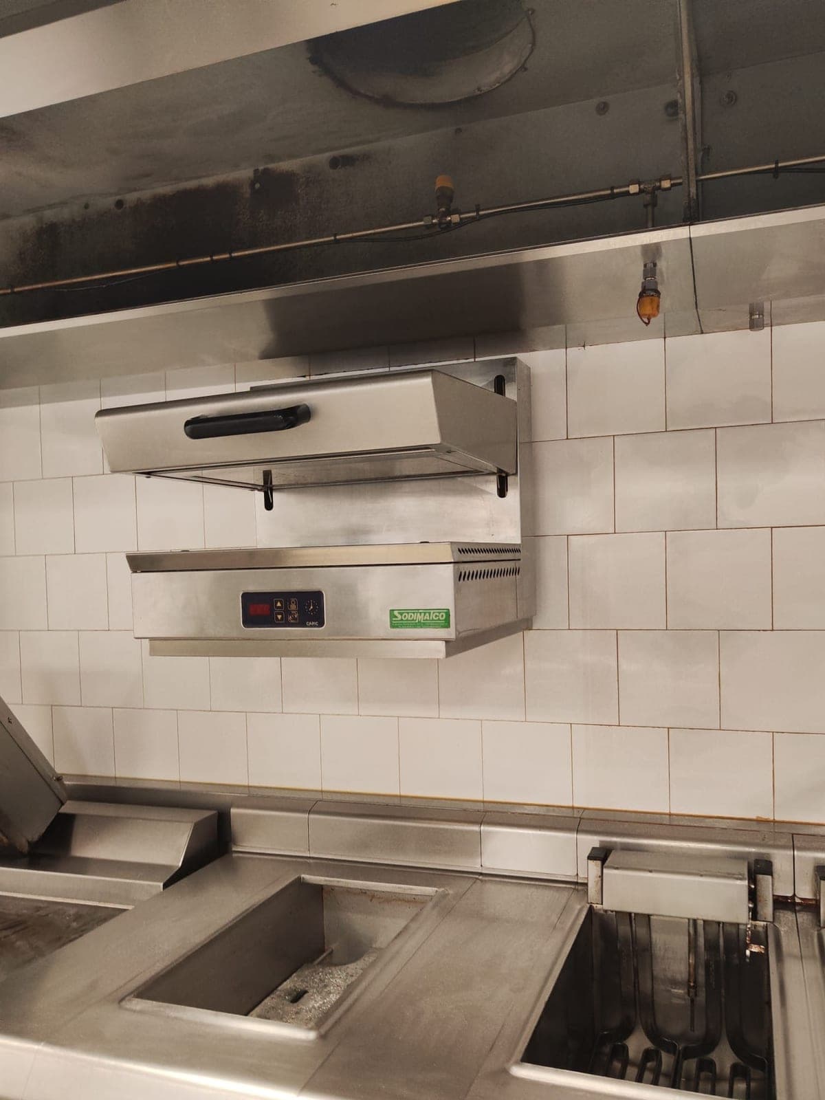 Hotte, salamandre et friteuses d'une cuisine de restaurant, inox et carrelage ternis par la graisse