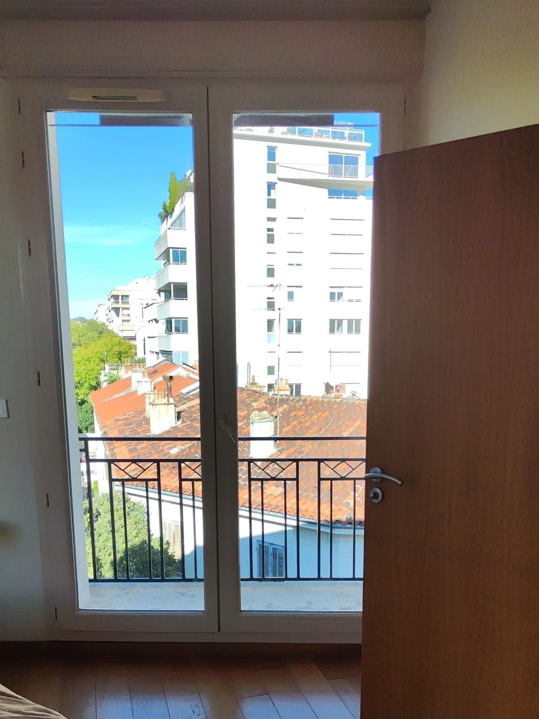 Appartement vide, parquet propre et porte-fenêtre ouverte sur le balcon