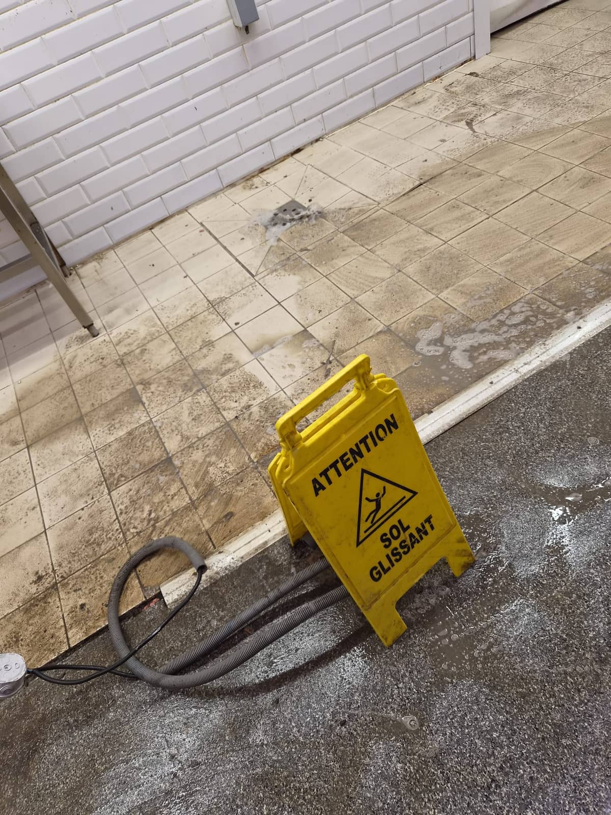 Arrière d'une surface commerciale, carrelage terni et panneau sol glissant